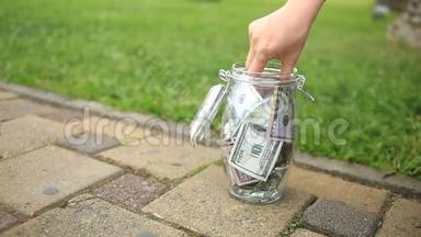 一个人从街上的玻璃罐里拿钱。 一个玻璃罐子里的钱